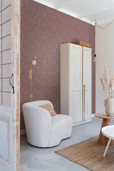 Vliestapete mit feinem floralem Muster in einem hellen, gemütlichen Wohnzimmer mit weißem Sessel, Holzschrank und Jute-Teppich.