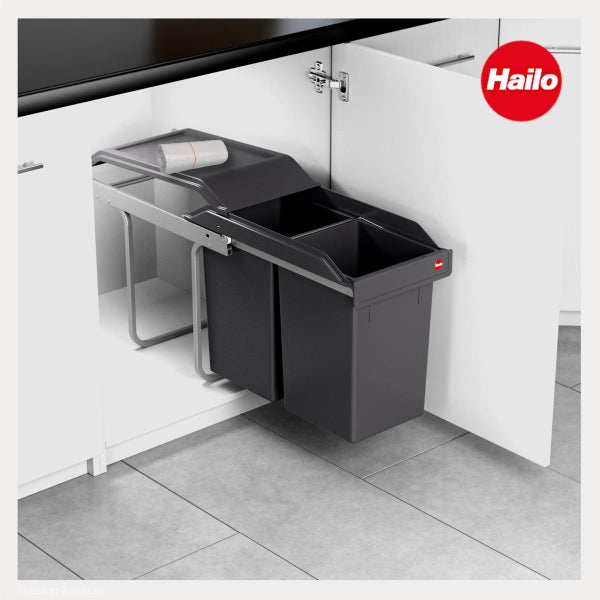 Hailo Logo. Einbau-Mülltrennsystem mit zwei grauen Abfalleimern in einem weißen Küchenunterschrank, ausziehbar auf Metallschienen.