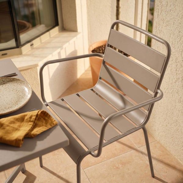Moderner Gartenstuhl aus Metall mit Armlehnen und Latten-Design auf einem hellen Balkon neben einem Bistrotisch.