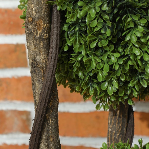 Nahaufnahme eines künstlichen Formschnittbaums mit grünen Blättern und einem Stamm mit spiralförmigem Dekor.