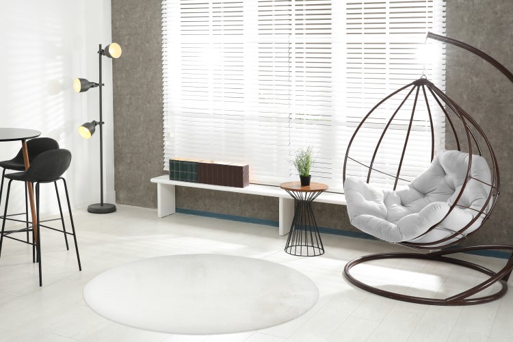 Ein moderner Wohnraum mit Hängesessel, Stehlampe, Bartisch mit Stühlen und einem Fenster mit Jalousien, hell und stilvoll eingerichtet.