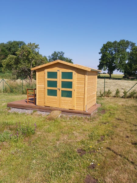 Gartenhaus aus Holz mit Satteldach und Doppeltür mit Glaseinsätzen auf einer Holzterrasse.