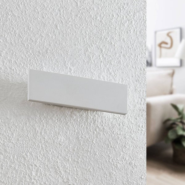 Rechteckige LED-Wandleuchte montiert an einer strukturierten weißen Wand in einem hellen Wohnzimmer.