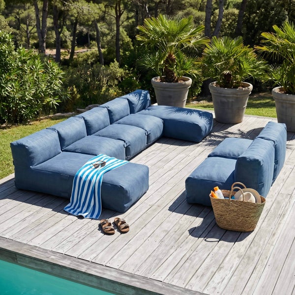 Modulares Gartenlounge-Set in Blau auf einer Holzterrasse am Pool, umgeben von Palmen und Gartenpflanzen.