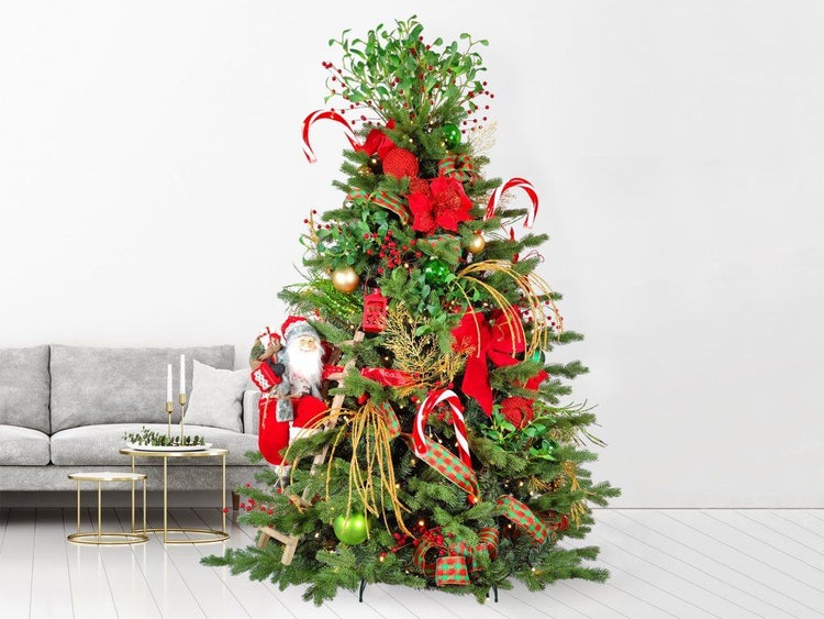 Geschmückter Weihnachtsbaum mit Kugeln, Schleifen, Zuckerstangen und Weihnachtsmannfigur in einem Wohnzimmer neben einem Sofa.
