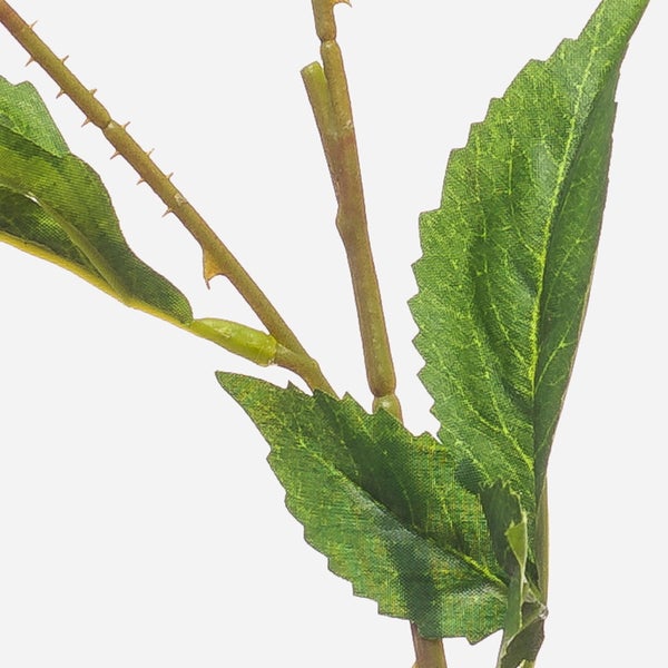 Detailaufnahme eines künstlichen Zweigs mit grünen gezackten Blättern und kleinen Dornen am Stiel.