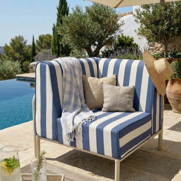 Blau-weiß gestreifter Loungesessel mit Zierkissen und Decke auf einer sonnigen Terrasse an einem Pool.