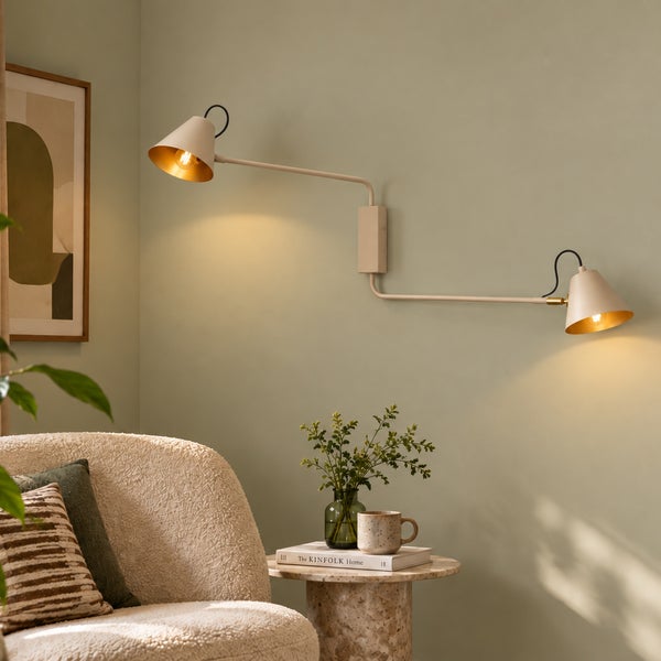 Moderne zweiflammige Wandleuchte mit schwenkbaren Armen in einem Wohnraum mit Sessel und Beistelltisch.