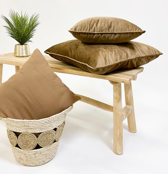Dekorative Szene mit zwei braunen Kissen auf einer Holzbank, einem Kissen in einem Korb und einer Pflanze in einem Topf.