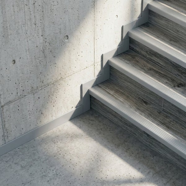 Treppenkantenprofil und Sockelleiste an einer Treppe in Holzoptik vor einer Betonwand.