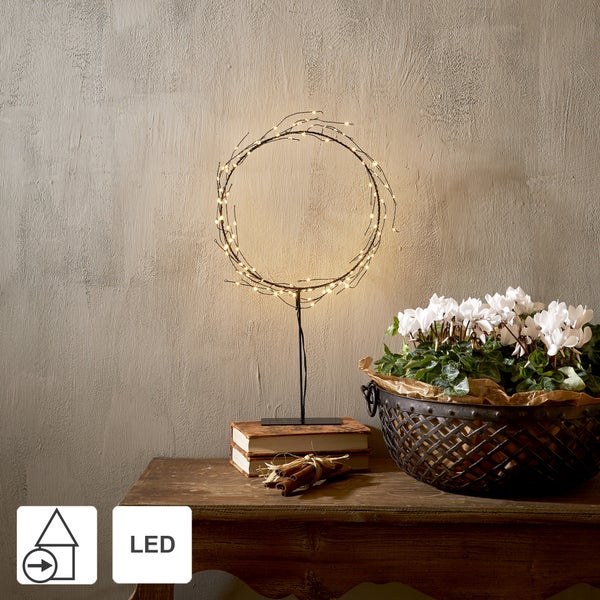 Dekorative LED-Tischleuchte in Ringform auf einem Holztisch mit Blumenschale und Büchern.