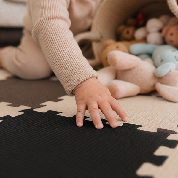 Ein Kleinkind spielt auf einer gepuzzelten Schaumstoffmatte mit weichen Plüschtieren, die aus einem Korb gefallen sind.