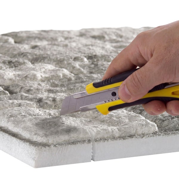 Eine Hand schneidet eine Strukturplatte aus Polystyrol mit einem Cuttermesser