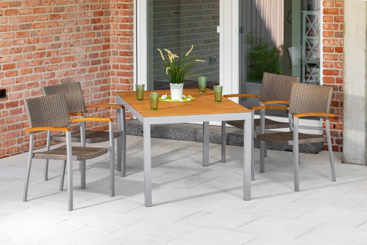 Modernes Garten-Set auf Terrasse mit quadratischem Tisch aus Holz und Metall sowie vier Rattanstühlen mit Holzarmlehnen vor einer Ziegelwand.