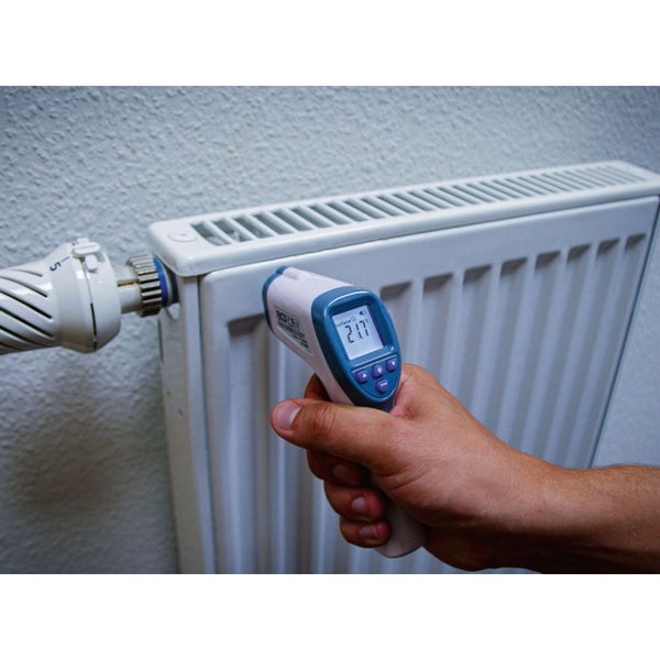 Eine Hand hält ein Infrarot-Thermometer, das die Temperatur eines Heizkörpers misst.