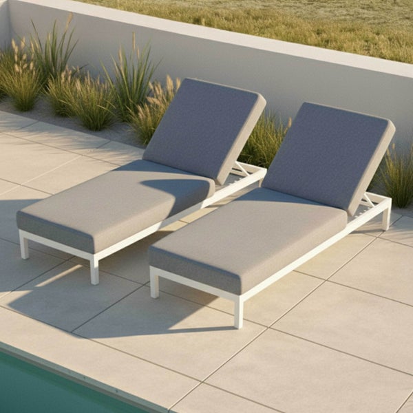 Zwei moderne Sonnenliegen mit weißem Aluminiumgestell und grauen Polstern auf einer gefliesten Terrasse am Pool.