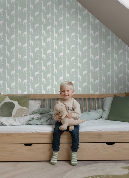 Kinderzimmer mit Giraffen-Tapete, Bett aus hellem Holz und lächelndem Kind mit Stofftier.