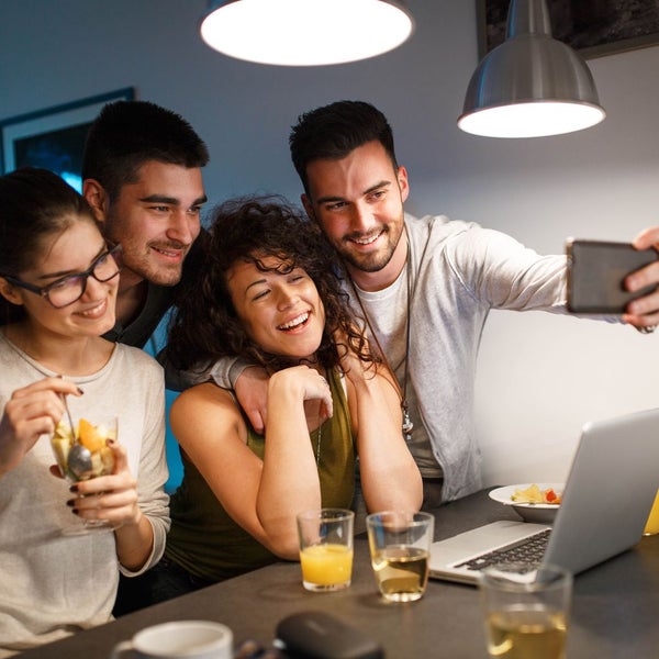 Moderne Innenbeleuchtung mit zwei Pendelleuchten über einem Tisch, an dem eine Gruppe von Personen sitzt und ein Selfie macht.