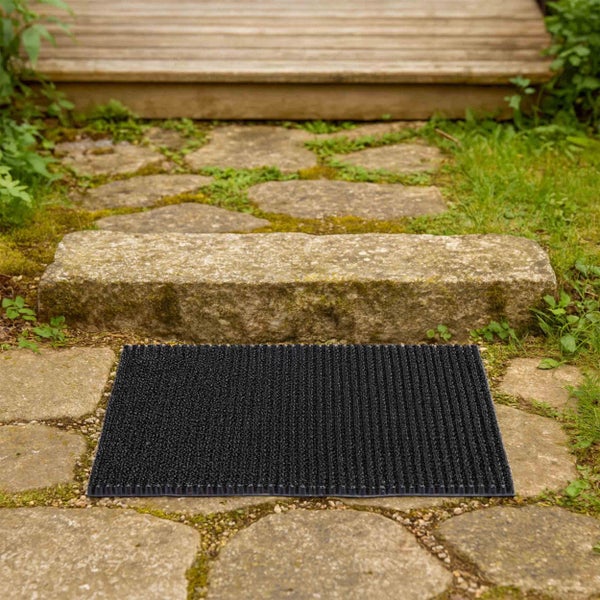 Schwarze Fußmatte auf einem steinernen Gartenweg.