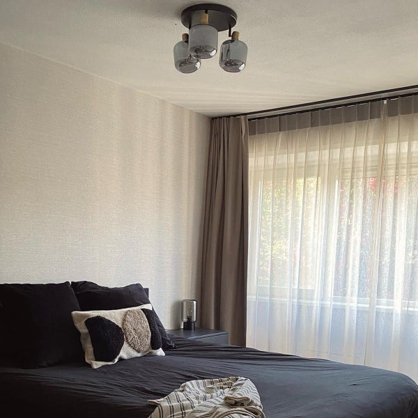 Deckenleuchte mit drei rauchfarbenen Glasschirmen in einem modernen Schlafzimmer mit dunklem Bett und hellen Vorhängen.