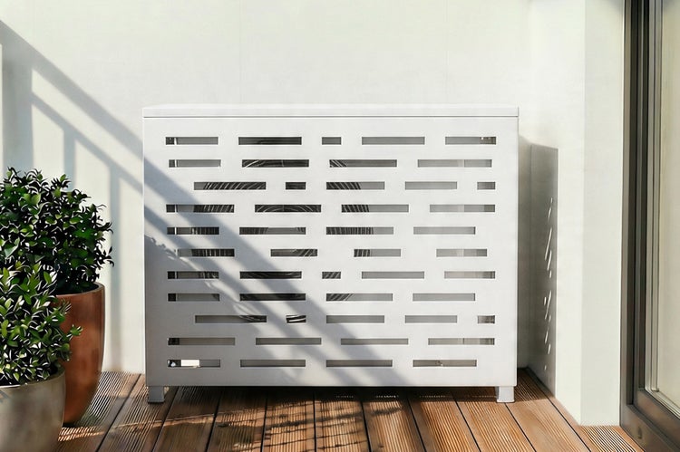 Moderne rechteckige Abdeckung für Klimaanlagen mit geometrischem Lochmuster auf einer Holzterrasse neben grünen Topfpflanzen in heller Umgebung.