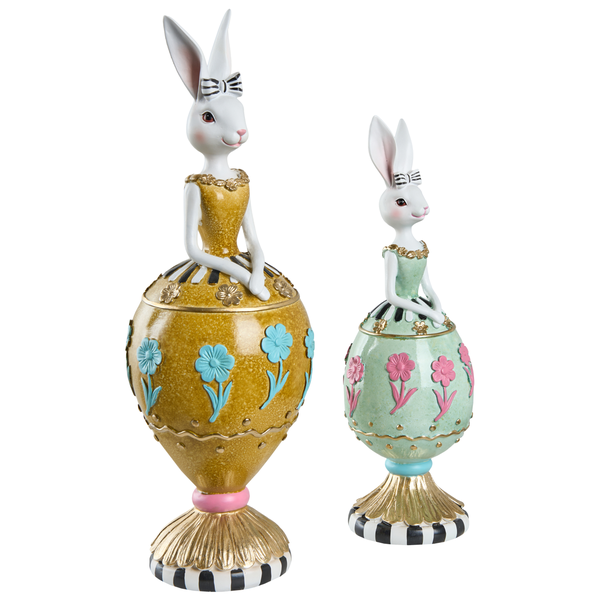 Zwei dekorative Osterhasen-Figuren aus Polyresin in gelben und grünen Kleidern mit Blumenmuster auf eiförmigen Sockeln.