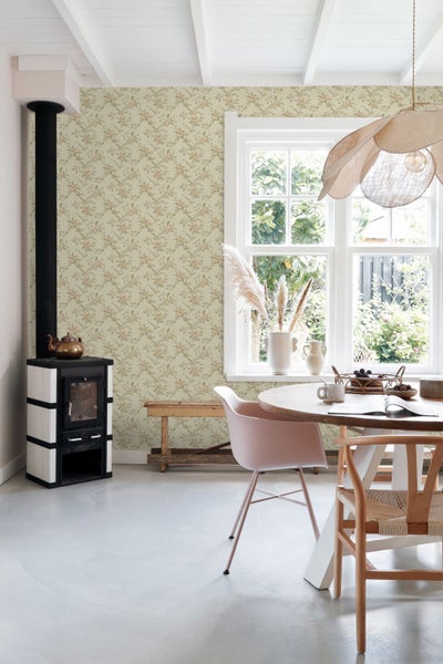 Helles Esszimmer mit floraler Mustertapete, schwarz-weißem Kaminofen und Holztisch vor großem Fenster im Landhausstil.
