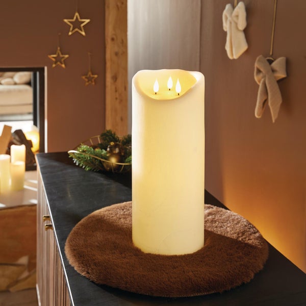 Große LED Stumpenkerze mit drei Flammen als stimmungsvolle Weihnachtsdekoration auf einem runden flauschigen Untersetzer in einem Wohnraum.