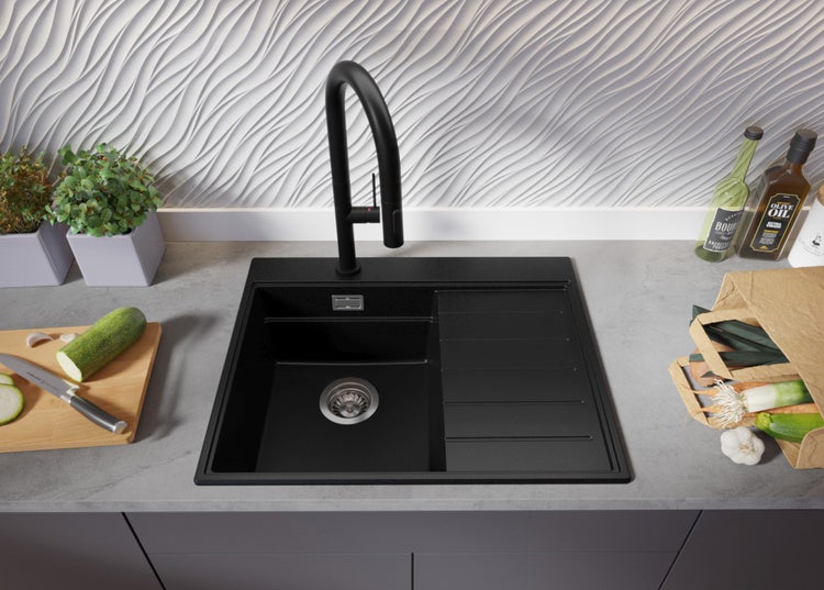 Schwarze Küchenspüle mit Abtropffläche und Armatur auf einer Arbeitsplatte mit Lebensmitteln