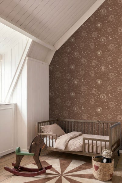 Kinderzimmer mit Tapete mit Sonnen-, Mond- und Sternmuster auf einer Dachschräge, Holzbett und Schaukelpferd in heller Atmosphäre.