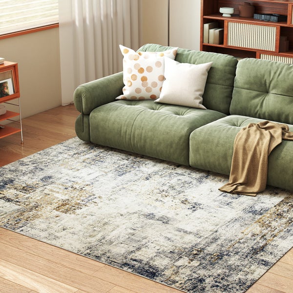 Rechteckiger Teppich mit abstraktem Muster im Used-Look in einem hellen Wohnzimmer mit grünem Sofa und Holzboden.