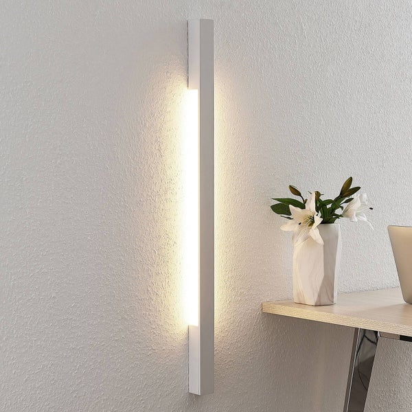 Moderne LED-Wandleuchte in schlankem Design an einer strukturierten Wand neben einem Schreibtisch mit Blumen, hell und organisiert.