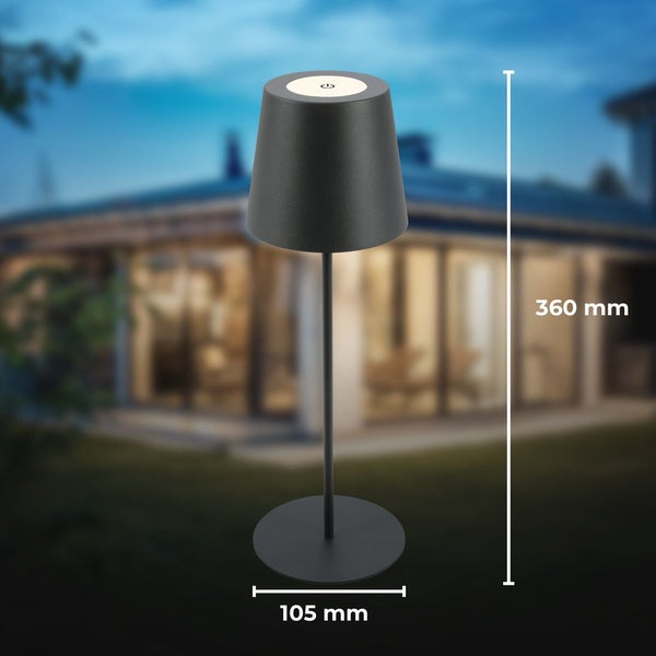 Schwarze Tischlampe für den Außenbereich mit Touch-Funktion, Höhe 360 Millimeter, Durchmesser 105 Millimeter, vor einem beleuchteten Haus.