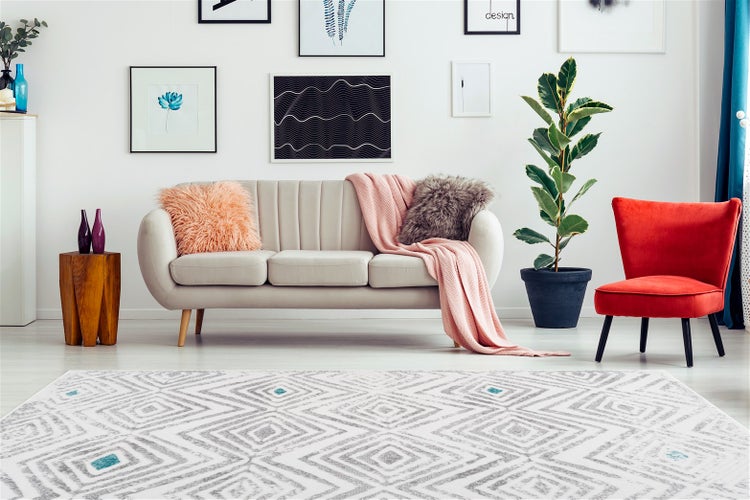 Helles Wohnzimmer mit beige Sofa, rotem Sessel und einem modernen Teppich mit geometrischem Rautenmuster in einem lichtdurchfluteten Raum.