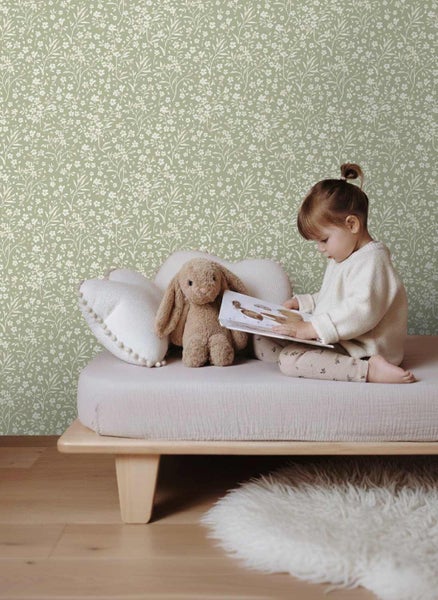 Vliestapete mit floralem Muster in einem hellen Kinderzimmer mit einem Kind auf einem Holzbett.