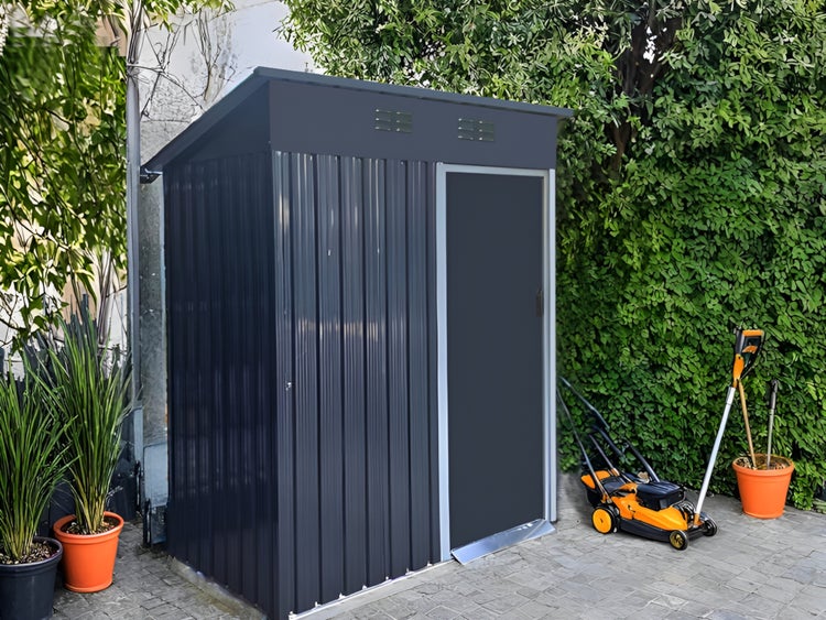 Modernes Metall-Gartenhaus in Anthrazit mit Pultdach und Einzeltür, auf einer Steinterrasse neben einem Rasenmäher und Gartengeräten stehend.