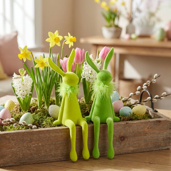 Osterdekoration mit zwei flauschigen Osterhasen in einem Holztablett mit Frühlingsblumen wie Narzissen, Tulpen und Hyazinthen sowie bunten Eiern.
