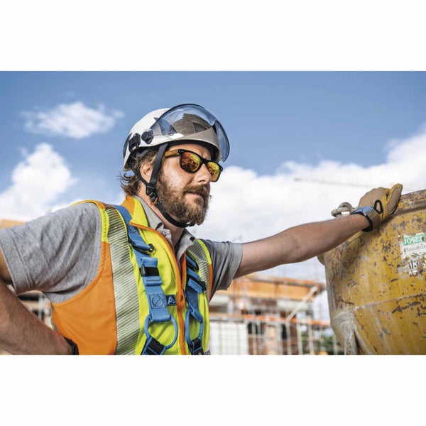 Bauarbeiter auf einer Baustelle mit weißem Schutzhelm, Visier, Sonnenbrille, Warnweste, blauem Auffanggurt und Arbeitshandschuhen.