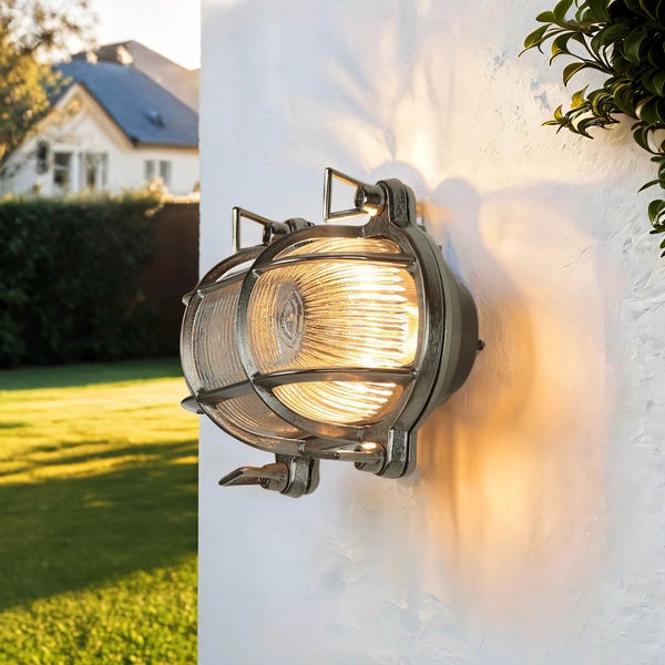 Eine Wandleuchte mit Schutzgitter und klarem Glas sorgt für Beleuchtung im Außenbereich.