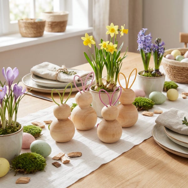 Festliche Osterdekoration mit Holzhasen, Frühlingsblumen wie Narzissen und Hyazinthen sowie verzierten Ostereiern auf einem gedeckten Holztisch.