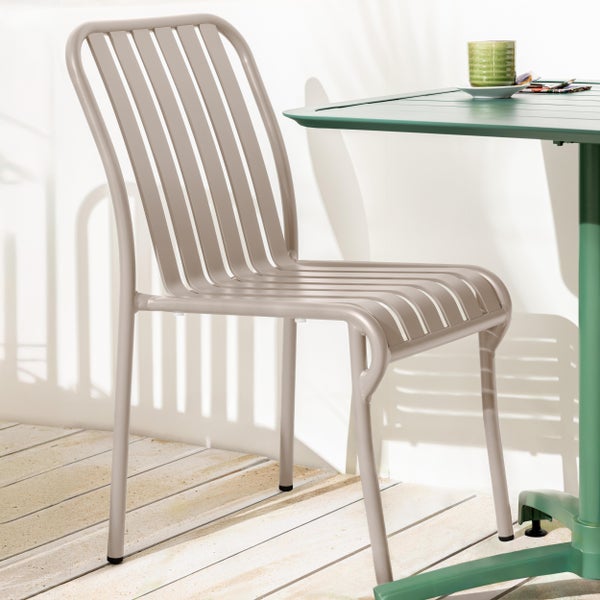 Moderner Gartenstuhl aus Metall mit Lattenstruktur neben einem Gartentisch auf einer hellen Holzterrasse.