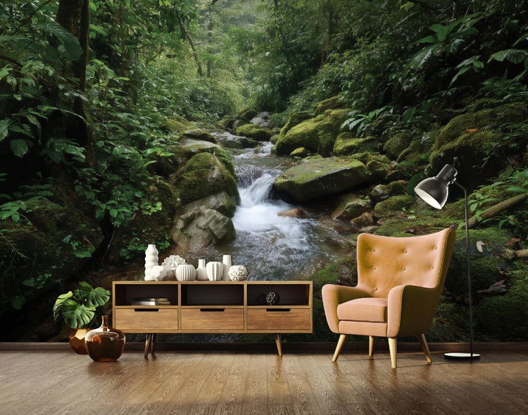 Fototapete mit Waldmotiv und Bachlauf, kombiniert mit einem Sideboard, einem Sessel und einer Stehleuchte in einem modern eingerichteten Raum.