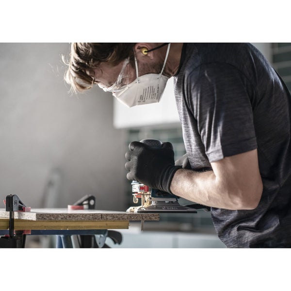 Ein Handwerker schleift ein Holzbrett mit einem Schleifgerät. Er trägt eine Schutzmaske, eine Schutzbrille und Handschuhe.