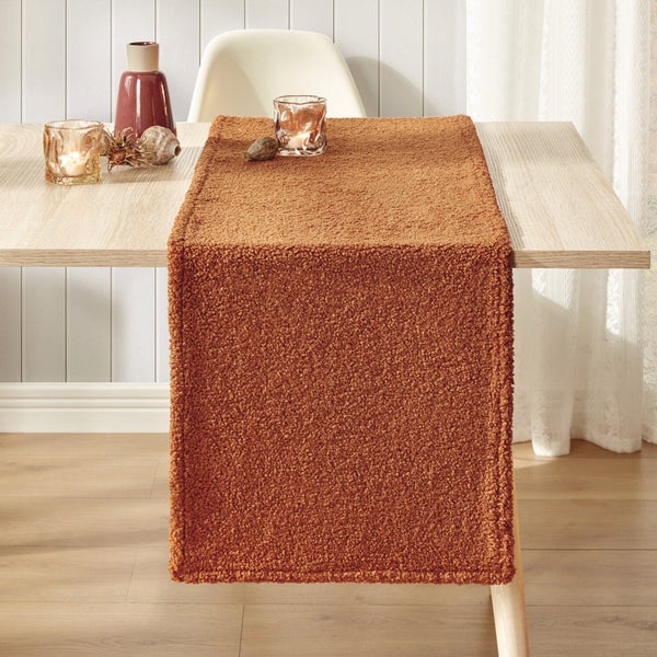 Dekorativer Tischläufer aus Stoff auf einem Holztisch mit Kerzen und Dekoration.