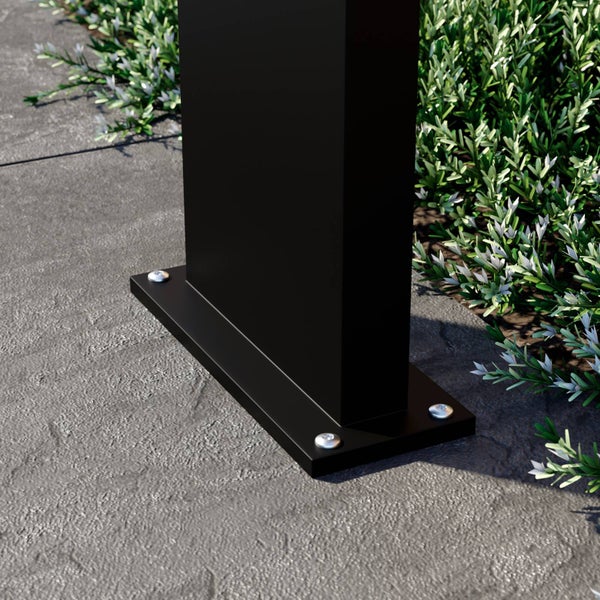 Schwarze Bodenplatte für einen Pfosten, verschraubt auf grauem Steinboden neben Grünpflanzen im Außenbereich.