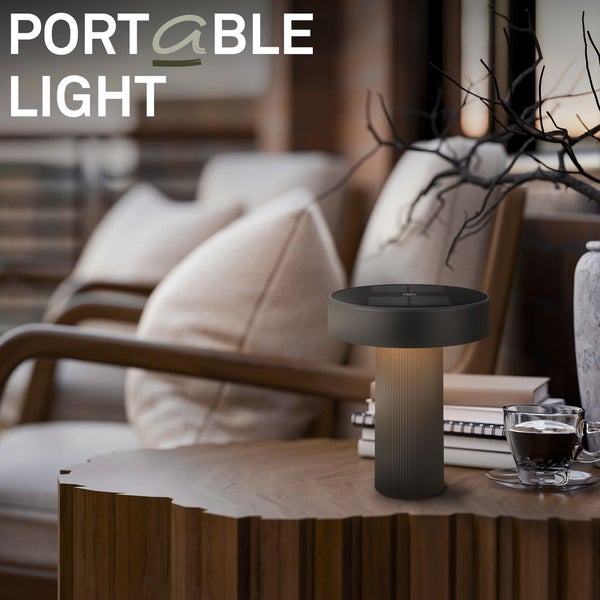 Moderne tragbare LED-Tischleuchte auf einem hölzernen Beistelltisch in einem hellen, organisierten Wohnzimmer mit Sessel und Kissen.