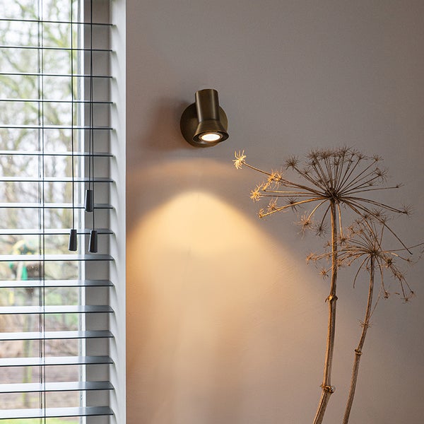 Wandleuchte aus Metall neben einem Fenster mit Jalousien und einer Dekoration aus getrockneten Blumen