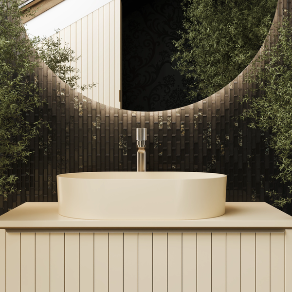 Modernes Badezimmer mit ovalem Aufsatzwaschbecken auf Waschtischunterschrank mit Lamellen, hoher Armatur, rundem Spiegel und dunklen Mosaikfliesen.