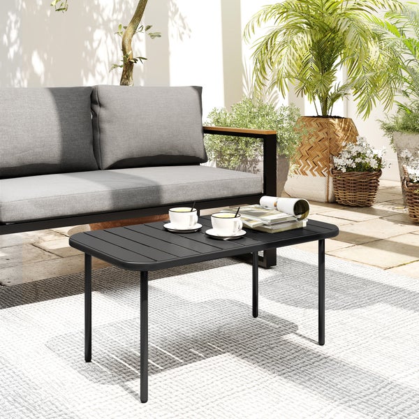 Moderner schwarzer Garten-Couchtisch aus Metall mit zwei Sesseln und grauen Polstern auf einer hellen Holzterrasse vor grünen Pflanzen.