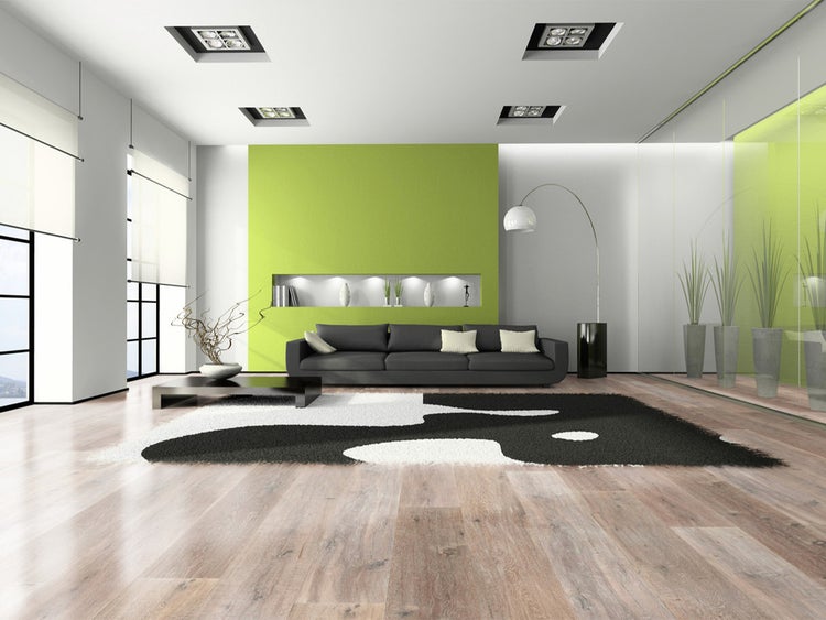 Modernes Wohnzimmer mit hellem Boden in Holzoptik, dunklem Sofa auf schwarz-weißem Teppich, einer grünen Akzentwand und Einbauleuchten.